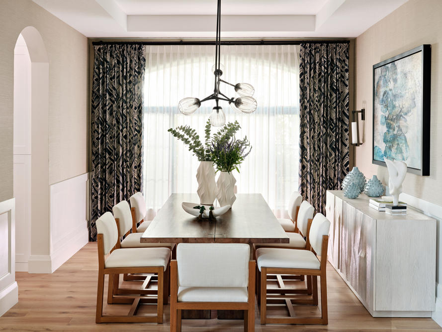 Dining room with long wood table, sculptural pendant lighting, layered drapery, sideboard, and abstract artwork.