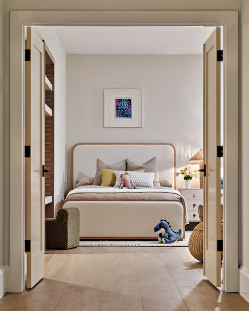 Child’s bedroom with upholstered bed, neutral bedding, playful accents, and double-door entry.