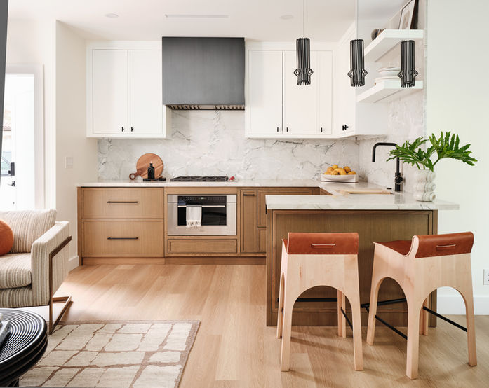 Modern guest house kitchen with wood and white cabinetry, charcoal range hood, marble backsplash, and sculptural bar stools.