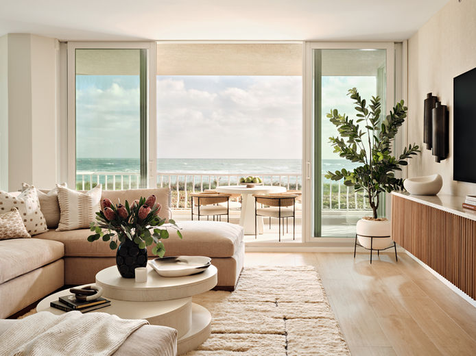 Coastal living room with neutral sectional, round nesting tables, ocean view, and floor-to-ceiling glass doors.