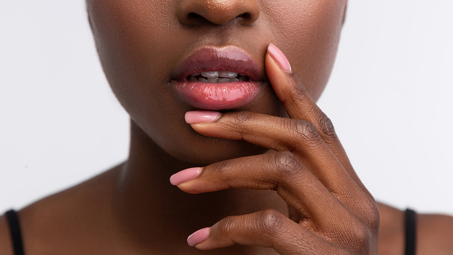 Image of a black women lips with lip stick and lip gloss on. This represent the SPMU dark lip neutralisation services available Apricity Aesthetics® - Brixton & Clapham, South London, England UK