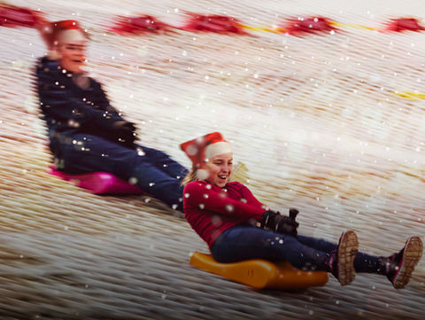 children toboggan down a slope wearing santa hats
