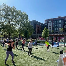 Group fitness class in the park with buildings in the background One Rule Dance.