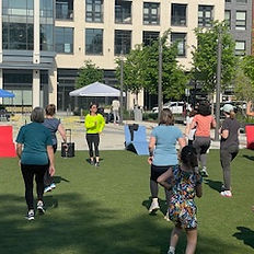 Group of people exercising on the grass in front of buildings outdoors.