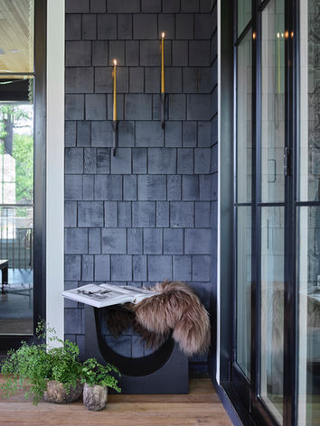 Sophisticated exterior home design with wall sconces, a low bench with a fur cushion, and potted plants that brings in warmth. Buckhead Atlanta interior designer. Bradley USA bench.