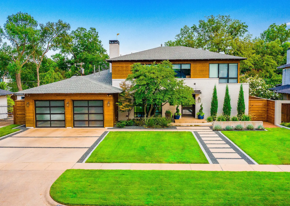 Contemporary front yard featuring lush green lawn, black gravel walkway with concrete stepping pads, minimal plant beds with agave and shrubs, modern edging, and stained wood accents on a residential home.
