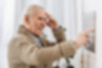 senior man looking at wall calendar and touching head.jpg