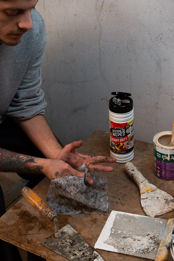Worker cleaning dirty hands with Hyper Wipes beside a 35-count canister in a workshop
