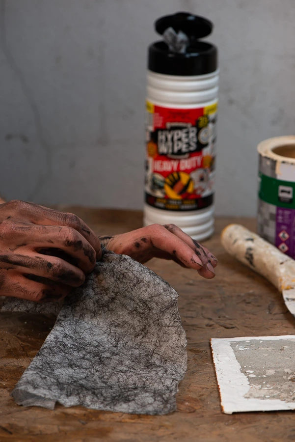 Close-up of dirty hands and a used textured wipe beside a Hyper Wipes canister