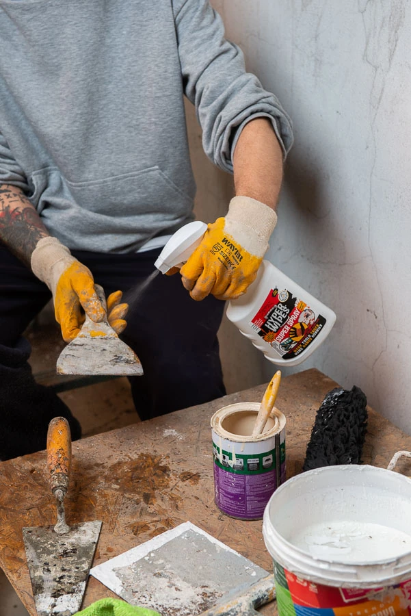 Worker applying Hyper Wipes Super Spray to a plastering tool in a workshop