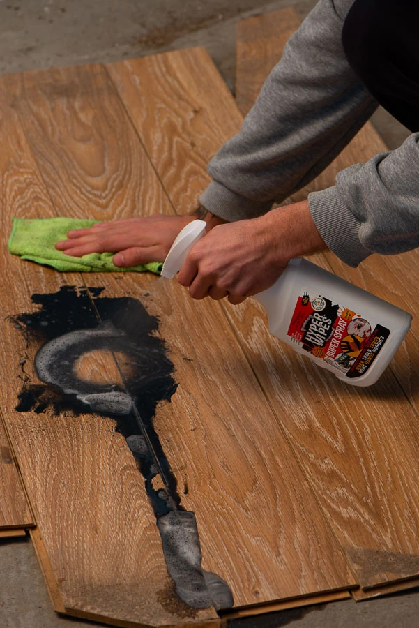 Worker using Hyper Wipes Super Spray and a green cloth on a dark stain on wood-look boards