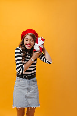 happy-girl-striped-shirt-denim-skirt-holding-red-gift-box-joyful-young-woman-with-wavy-hai