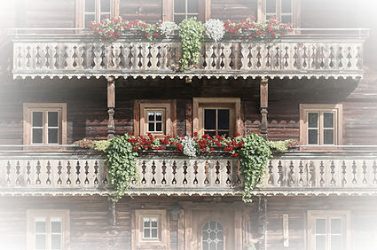 Typischer alpenländischer Balkon mit reichlicher Verzierung durch rote, grüne und weiße Pflenzen vor einer rustikalen Holzfassade