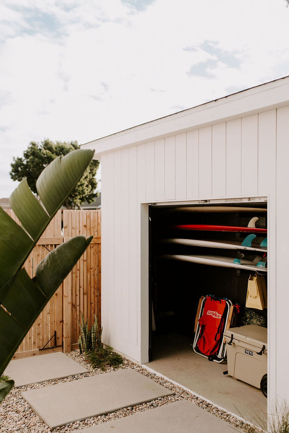 A modern white shed with colorful surfboards, beach chairs, fins and cooler neatly inside.