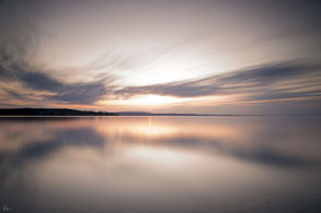 Sonnenuntergang über spiegelglattem See mit sanften Wolken und Reflexionen