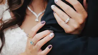 Bride's hands with rings embracing groom's arm on wedding day.