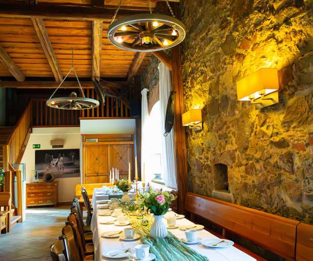 Festlich eingedeckte Tischtafel mit Blumenstrauß, rustikalem Leuchter und beleuchteter Bruchsteinmauer in modern-rustikalem Ambiente