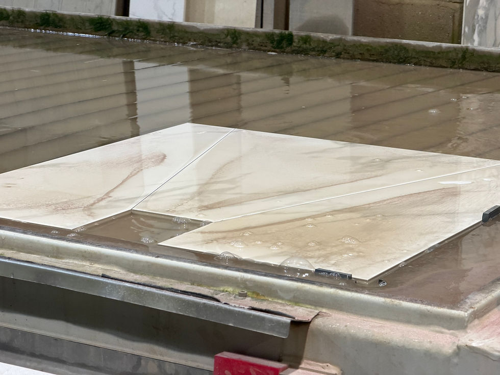 Close-up of water jet cutting in progress on large-format shower former tiles, showing precise diagonal cuts with water stream and tile secured on the machine bed at Affordable Granite's facility.