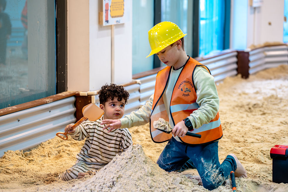 Children playing in a sandbox with construction toys.