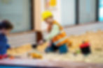 Child in a hard hat and safety vest playing in a sandbox.