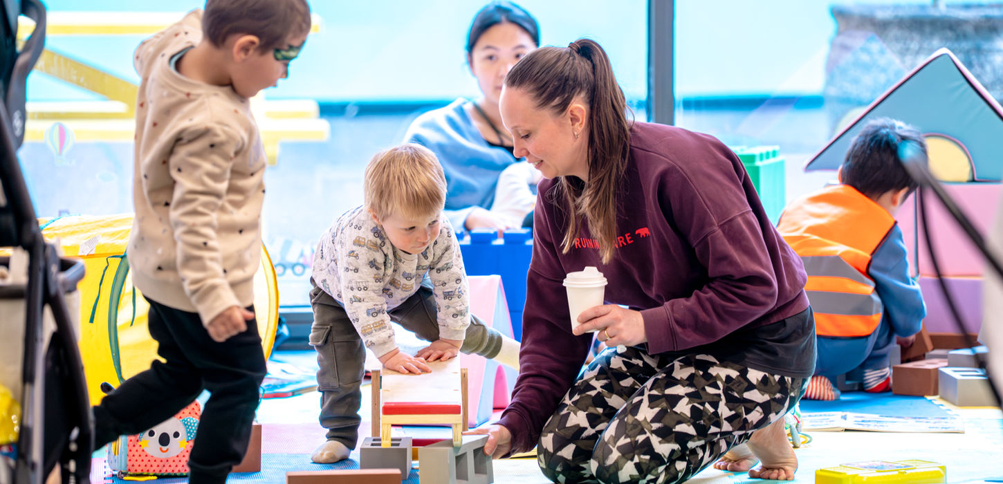Teacher playing with toddlers in a classroom gallery.