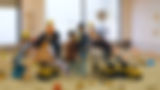 Children in safety vests playing with toy trucks in a sandbox.