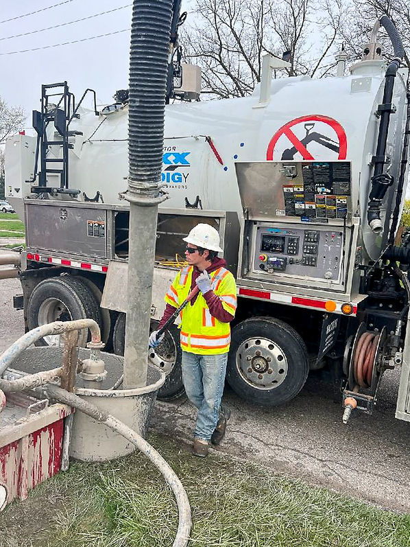 Worker in high visibility vest operating a well drilling truck with complex machinery, managing hose equipment for underground work.