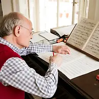 Elderly man writing music on sheet with pencil in bright room