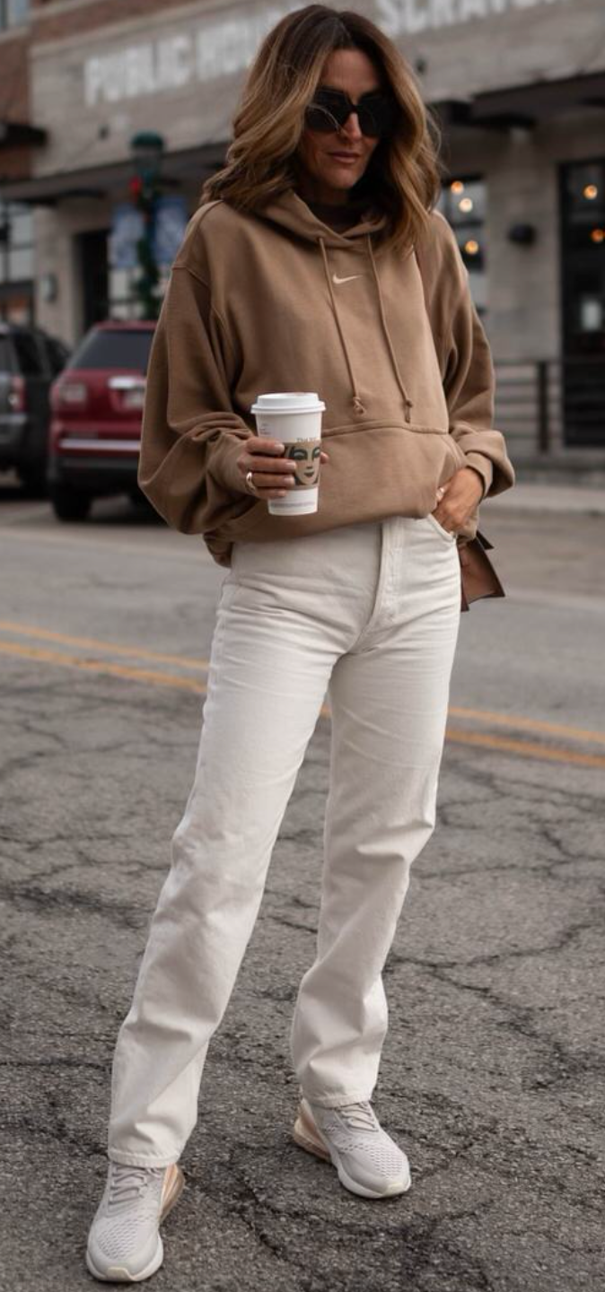 outfit printemps-sportif raffiné Femme portant un pantalon blanc, un sweat à capuche marron clair et des baskets