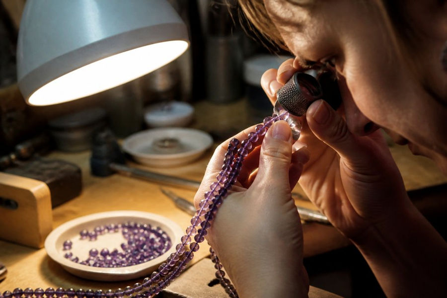 Jeweler inspecting faceted bead hole quality against gemstone bead standards using a magnifying loupe