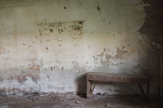 In een oude verlaten werkplaats staat nog een simpel houten bankje tegen de muur.