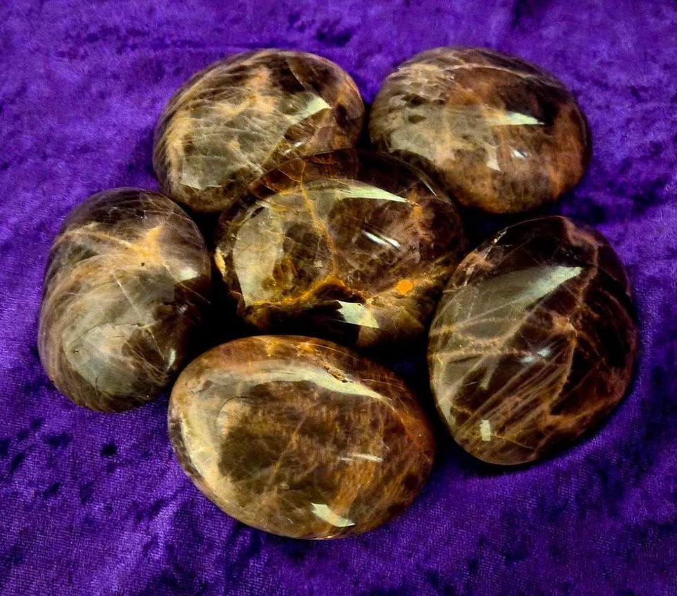 Polished black moonstone palm stones with silvery flashes and light streaks, arranged on a deep purple fabric background.