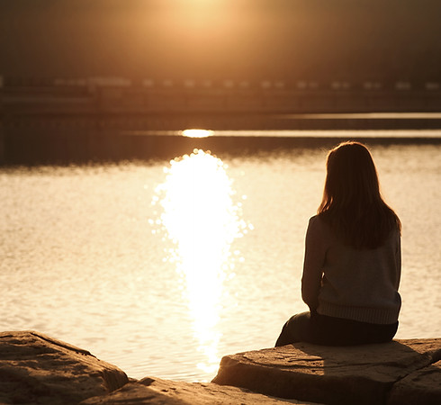Femme assise face à l’eau au coucher du soleil dans un moment d’introspection et de bien-être