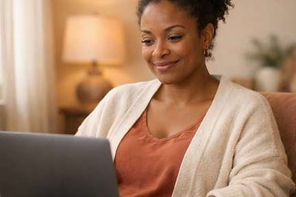 A woman smiles softly while on her laptop during an online therapy session from the comfort of her living room.