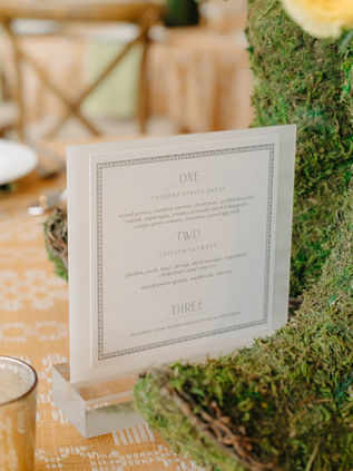 Bespoke table menu in a glass frame, nestled inside a unique moss-covered centerpiece base.