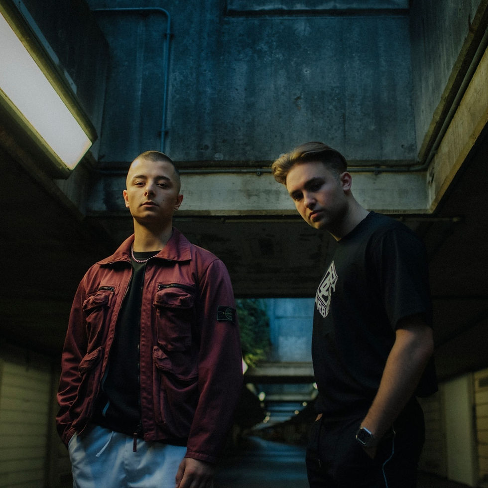 Prospa in a tunnel with concrete walls; one is wearing a burgundy jacket, the other a black T-shirt. Calm atmosphere, low lighting.