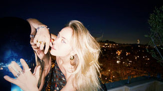 Elizabeth Lip with long blonde hair against a night-time city backdrop. She is wearing a sparkling dress and jewellery, looking into the camera with a thoughtful expression.