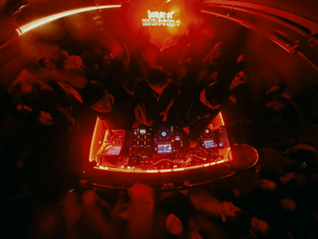 MNEEMO (Yaroslav Gorovoy) performing at a club with a glowing red-lit console. Crowd surrounds, enjoying the music. "house of vansnemo" text is visible above.
