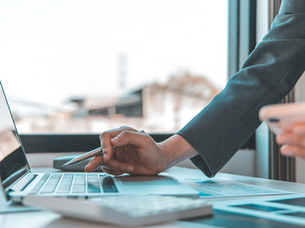 A professional woman multitasks with a laptop and smartphone, surrounded by financial documents and a calculator. Perfect for topics on business analysis, digital tools, remote work, and productivity in a modern office setting.