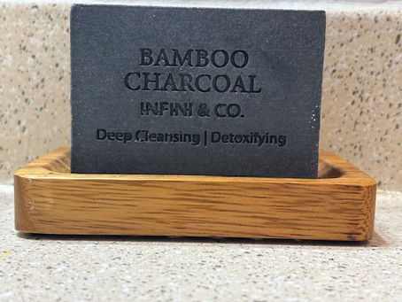 Artisanal Bamboo Charcoal soap bar by Infini & Co. on a wooden dish, labeled Deep Cleansing and Detoxifying.