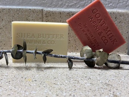Infini & Co. Rose Clay and Shea Butter soap bars styled with a botanical sprig on a rustic wood surface.