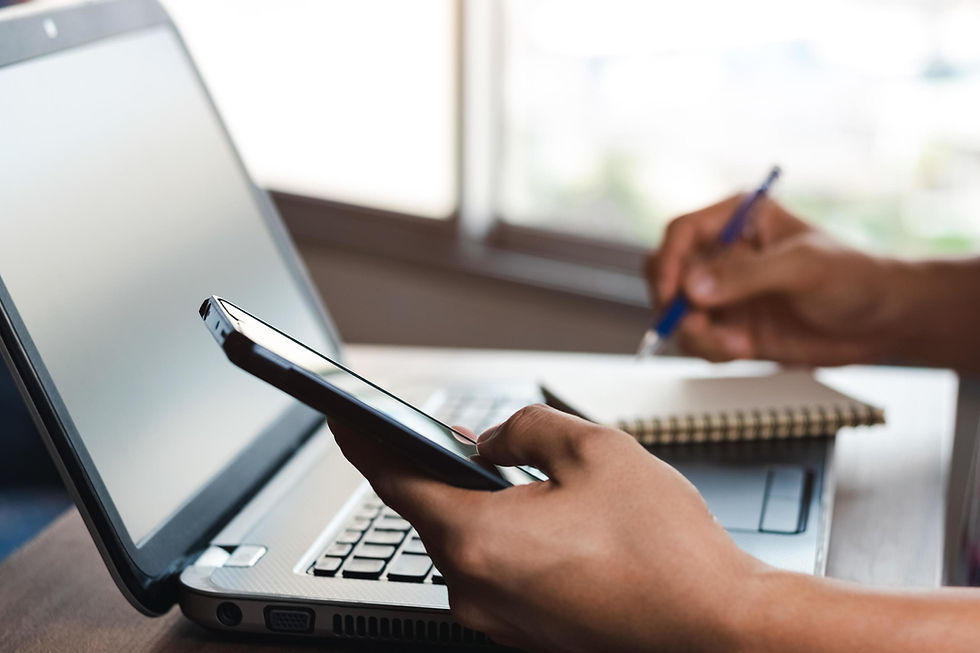 Person using a phone while working on a laptop and writing notes, illustrating ADHD attention challenges and difficulty focusing on simple tasks