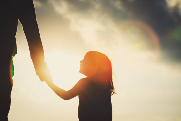 Parent holding a child’s hand at sunset, representing connection and parental love