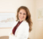 Jaimie Zaki, Wichita Falls doula and lactation consultant, stands in office wearing maroon shirt and white jacket with images on wall of fetal growth and development 