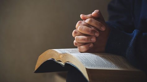 Praying with clasped hands on a Bible