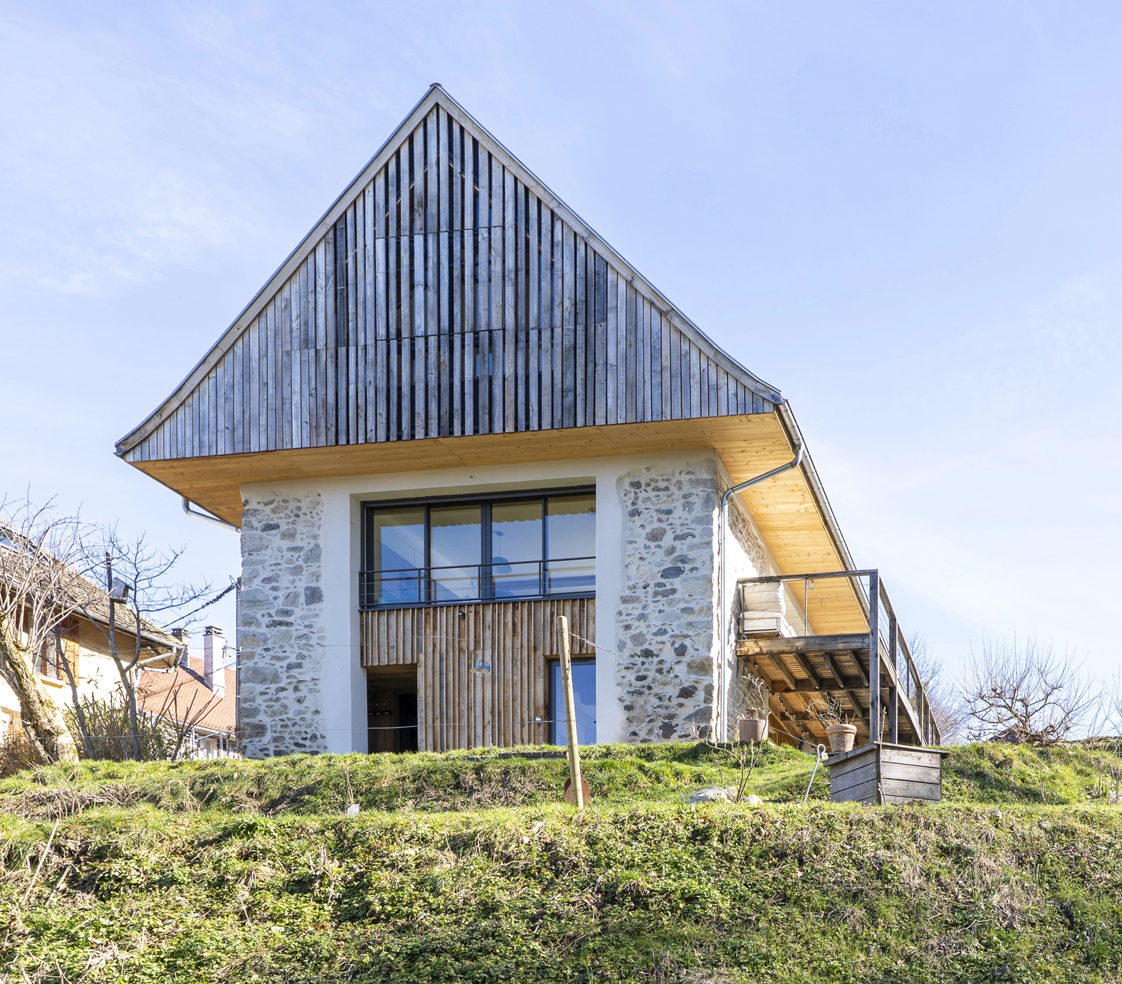 Façade principale du projet Re-Naissance Vernaculaire à Saint-Martin-d'Uriage : mur en pierre, bardage bois de réemploi et ouverture contemporaine. Lauréat prix construction bois réhabilitation 2026. Photo A. Frénot.