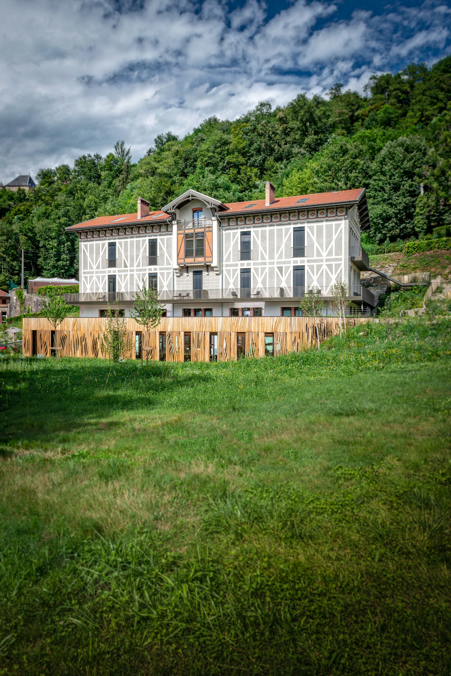 Vue panoramique de l'extension bois châtaignier de La Maison Aribert depuis la prairie, bâtisse patrimoniale du XIXe siècle en arrière-plan, Uriage-les-Bains. Atelier Joëlle Personnaz architecte. Photo D. Richalet.