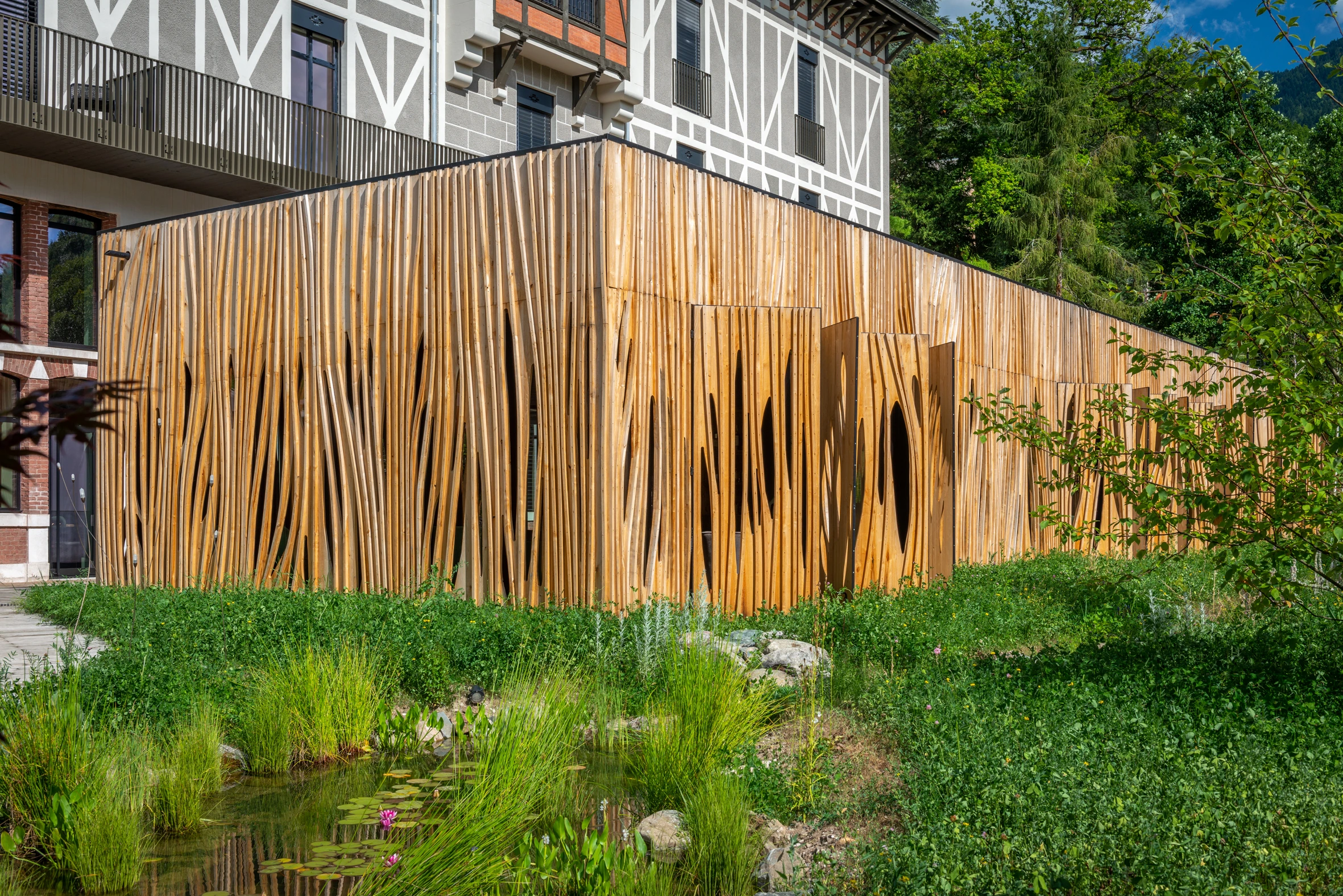 Extension bois de La Maison Aribert : bardage sculpté en châtaignier massif et pièce d'eau naturelle, Uriage-les-Bains. Projet lauréat Prix régional construction bois 2020. Photo D. Richalet.