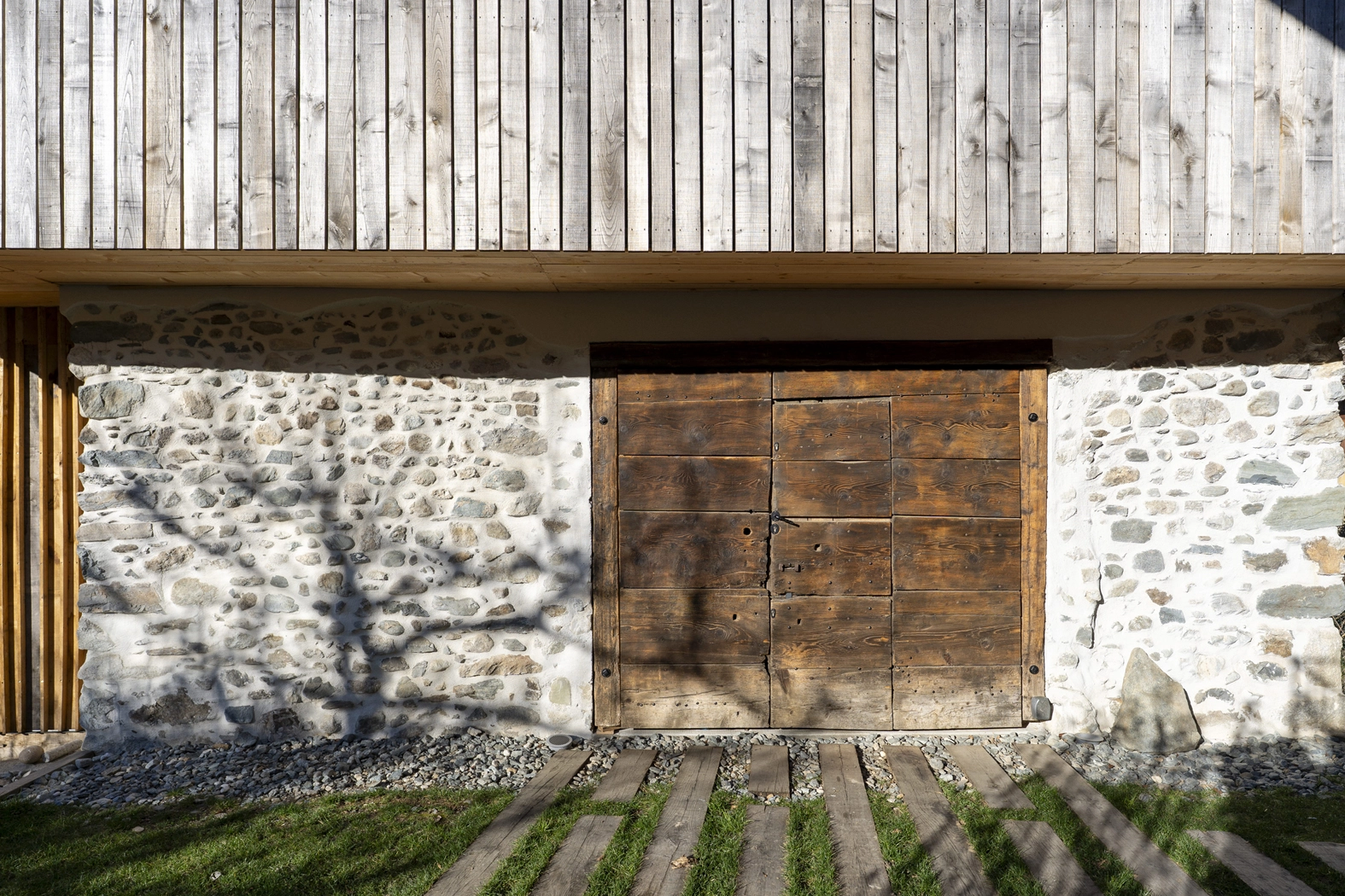 Détail de la façade du projet Re-Naissance Vernaculaire : mur en pierre restauré, porte ancienne de réemploi et bardage bois, Saint-Martin-d'Uriage. Atelier Joëlle Personnaz architecte. Photo A. Frénot.