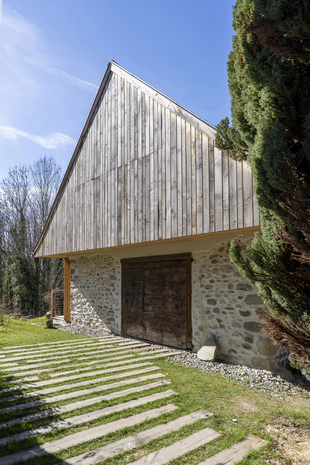   Pignon du projet Re-Naissance Vernaculaire : bardage vertical en bois de réemploi, porte ancienne conservée et cheminement en traverses bois, Saint-Martin-d'Uriage. Atelier Joëlle Personnaz architecte. Photo A. Frénot.